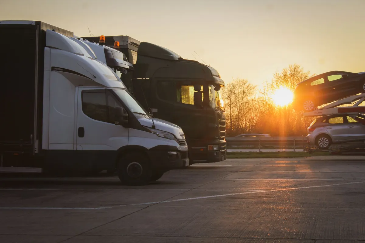 Rastplatz an der Fernstraße bei Sonnenuntergang mit weißem Kastenwagen, dunkler Sattelzugmaschine und einem Autotransporter