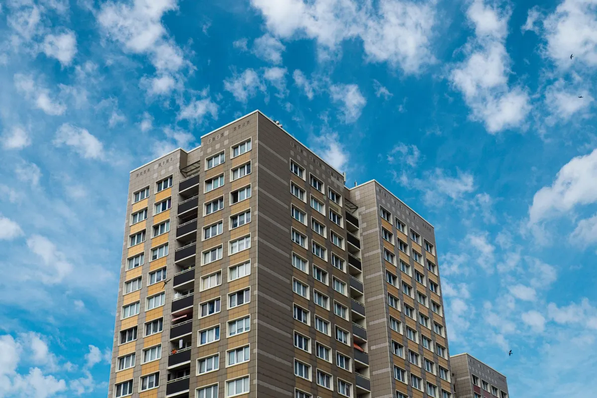 Mehrgeschossiges Wohnhochhaus aus den Siebzigern mit hellen Balkonen und Plattenfassade vor blauem Himmel mit Wolken