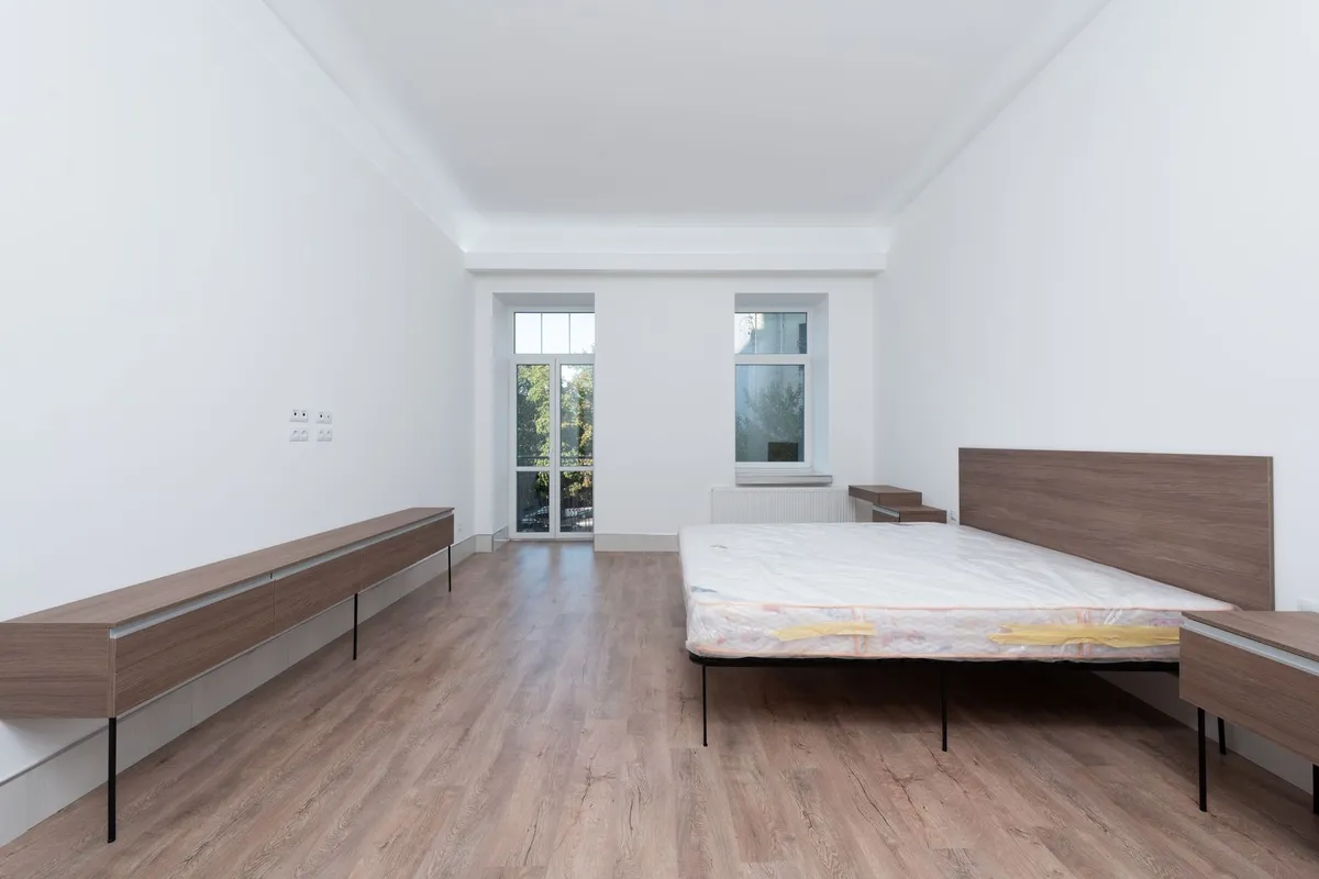 Leergeräumtes Zimmer beim Auszug: nacktes Bettgestell mit abgeklebter Matratze, Sideboard und Balkontür, Boden frei für den Umzug